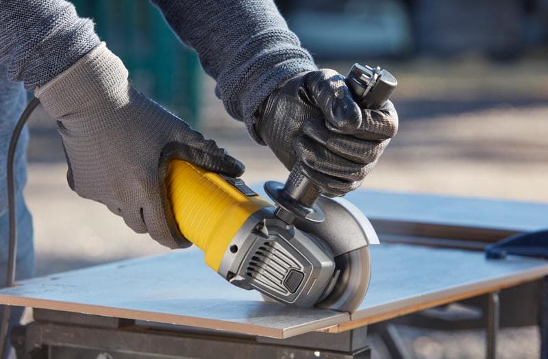 STANLEY FMEG210K meuleuse angulaire en utilisation, jaune et noire, coupe de carreau sur établi.