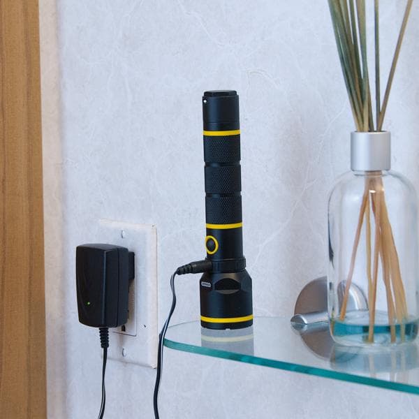 STANLEY 95-154 lampe de poche rechargeable noire et jaune en charge sur une étagère en verre, vue latérale.
