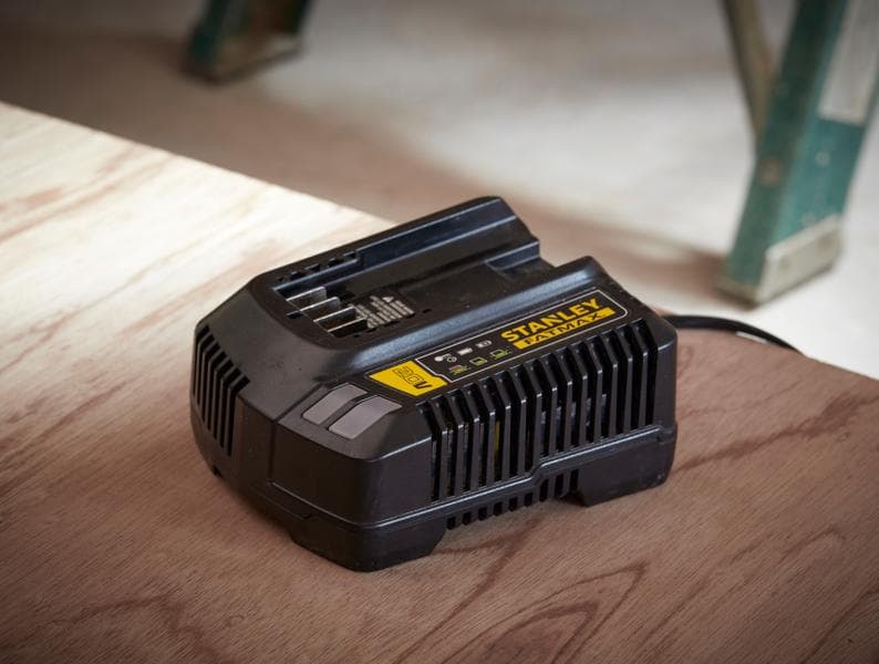 Photo du chargeur de batterie noir STANLEY SFMCB14 sur une surface en bois, étiquette FATMAX, en atelier.