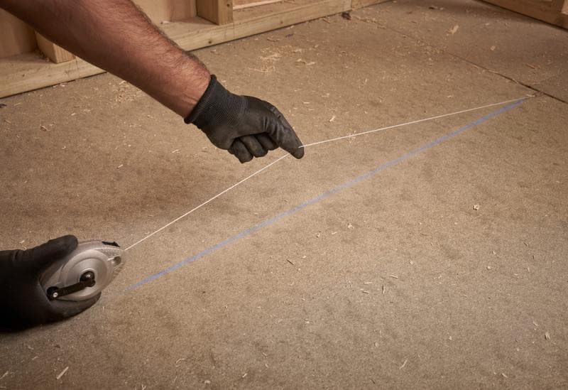 STANLEY 0-47-100 enrouleur de corde à tracer utilisé, mains gantées traçant une ligne droite bleue sur le sol.