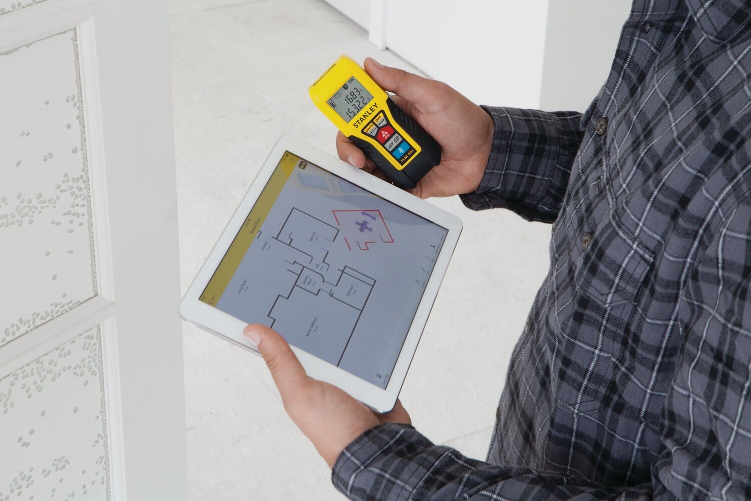 STANLEY STHT77343 télémètre laser tenu avec tablette présentant un plan de sol, environnement intérieur.