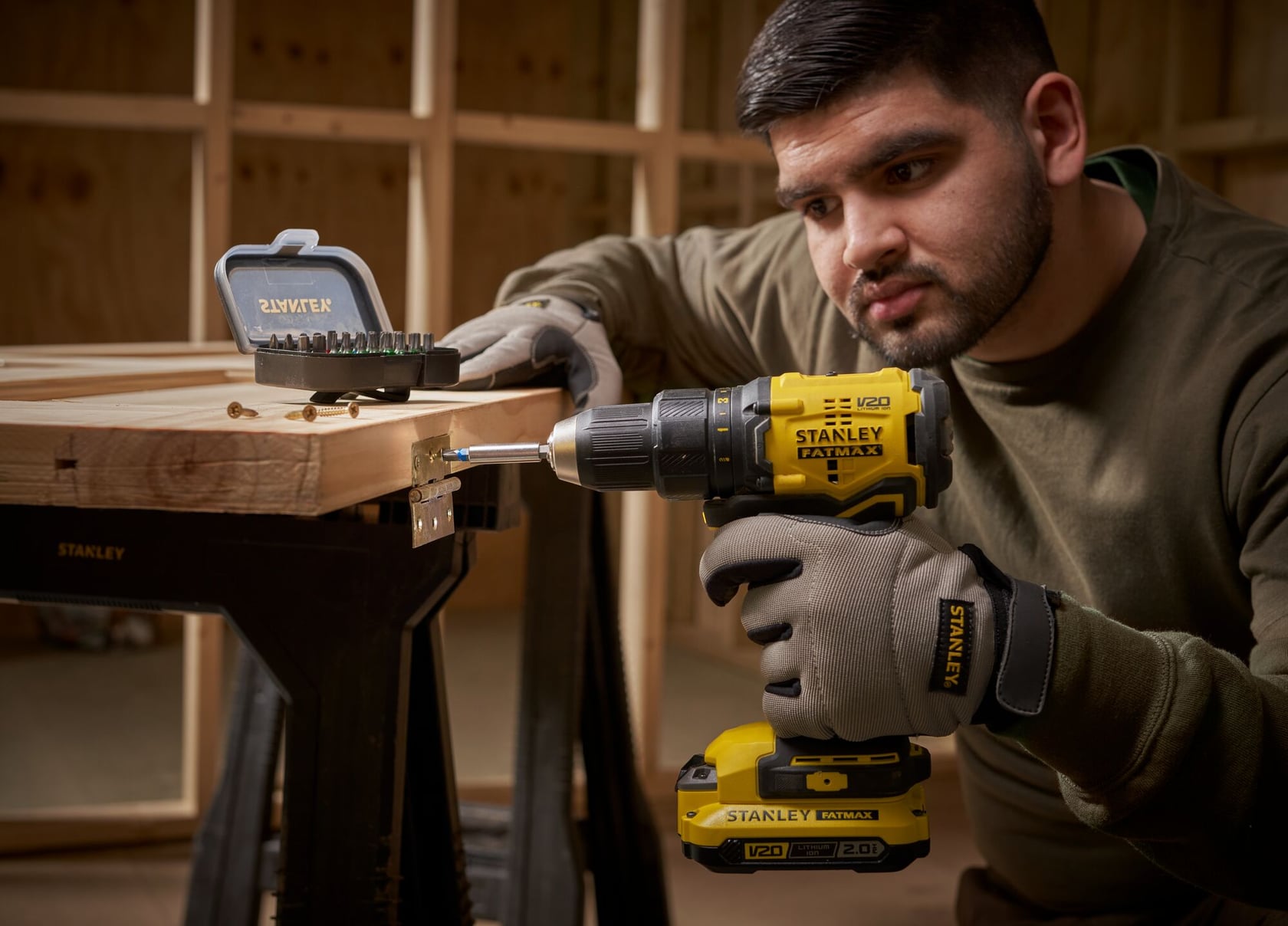 STANLEY STA60490 perceuse sans fil utilisée pour assembler du bois sur un établi, coffret de forets visible, atelier en arrière-plan.