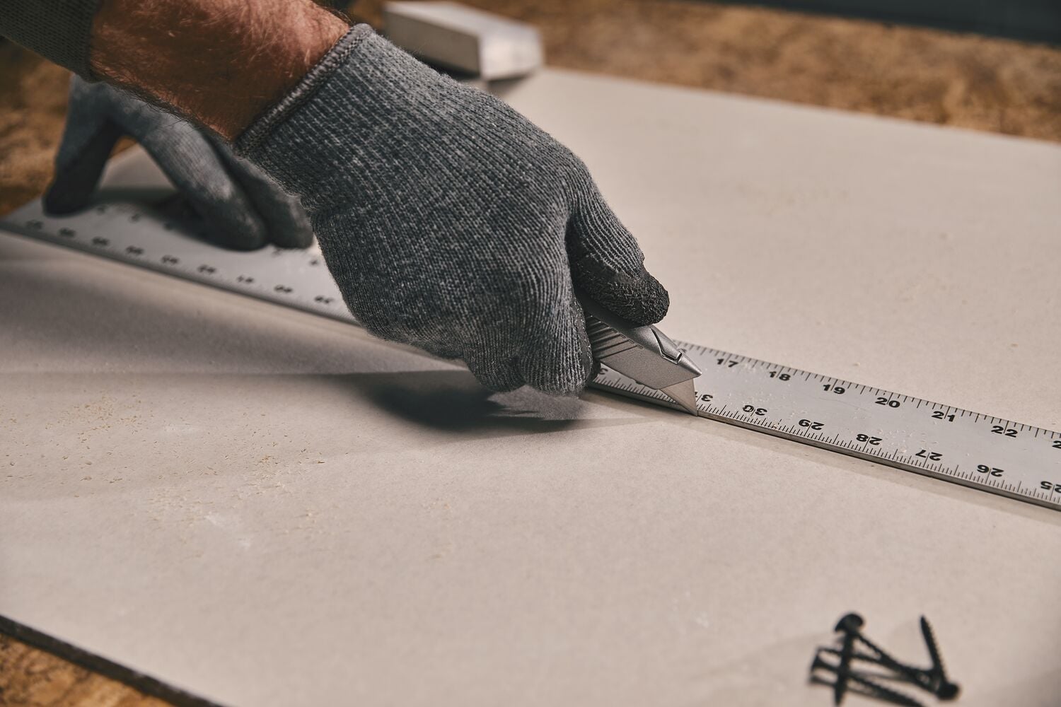 Cutter STANLEY 10-299 découpant le long d'une règle métallique sur une plaque, gros plan main gantée.