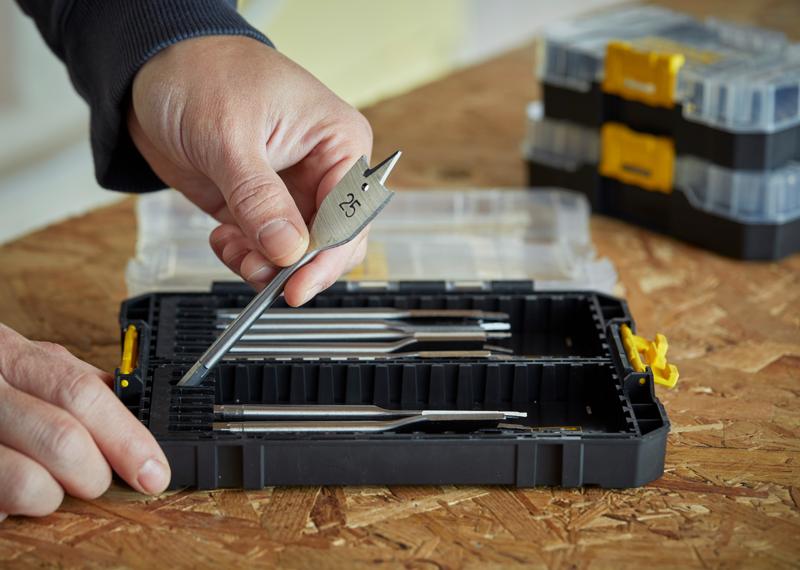STANLEY STA88556 coffret de forets dans une boîte noire, main tenant un foret plat pour bois, boîte ouverte sur surface en bois.